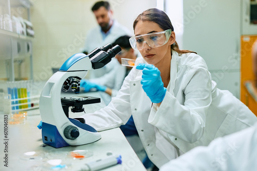 Young female scientist analyzing test sample while working with microscope in lab.