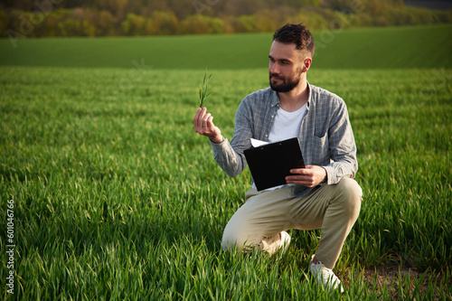 With notepad in hands. Handsome young man is on agricultural field