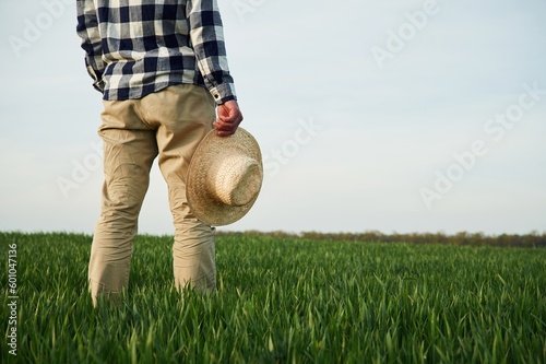 Rear view. Standing and holwing straw hat in hand. Young man is on agricultural field photo