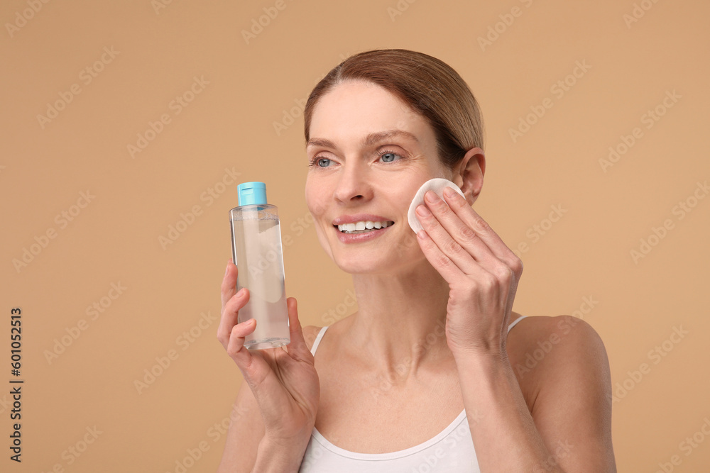 Beautiful woman removing makeup with cotton pad on beige background Beautiful woman removing makeup with cotton pad on beige background