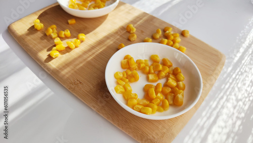 Lot of pieces of canned yellow corn on plate which is on wooden bamboo cutting board on white background. The concept of cooking and delicious healthy food