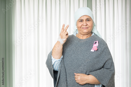 Fotografie Portrait of indian senior woman cancer patient survivor standing with victory hand gesture at hospital after chemotherapy sessions , Healthcare Concept
