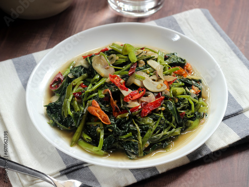 Stir-fried Water Spinach (Tumis Kangkung) is one of Indonesian Daily Menu and Favorite Food. Served on white plate on rustic blue wooden table