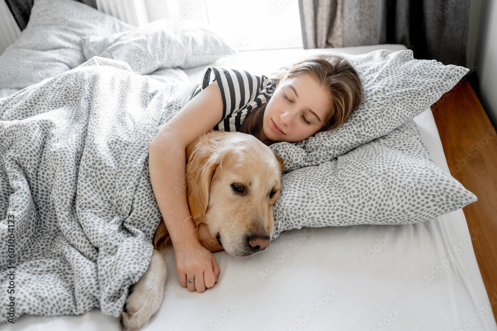 Pretty girl hugging golden retriever dog and sleeping in bed. Female teenager with purebred doggy pet labrador resting napping together Pretty girl hugging golden retriever dog and sleeping in bed. Female teenager with purebred doggy pet labrador resting napping together