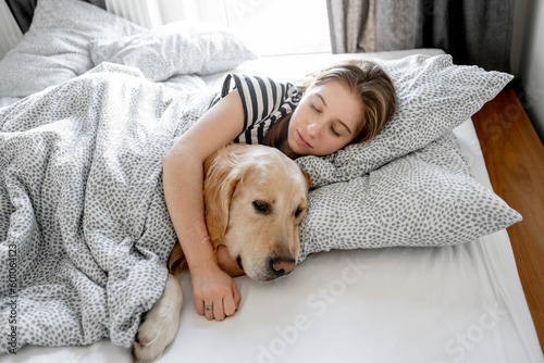Pretty girl hugging golden retriever dog and sleeping in bed. Female teenager with purebred doggy pet labrador resting napping together