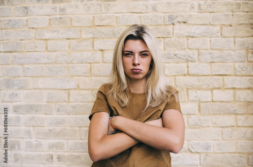 Discontent young woman standing near brick wall - obrazy, fototapety, plakaty 