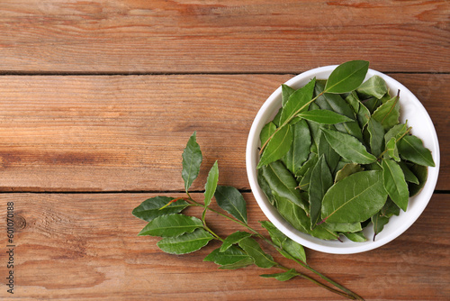 Aromatic fresh bay leaves and bowl on wooden table, flat lay. Space for text