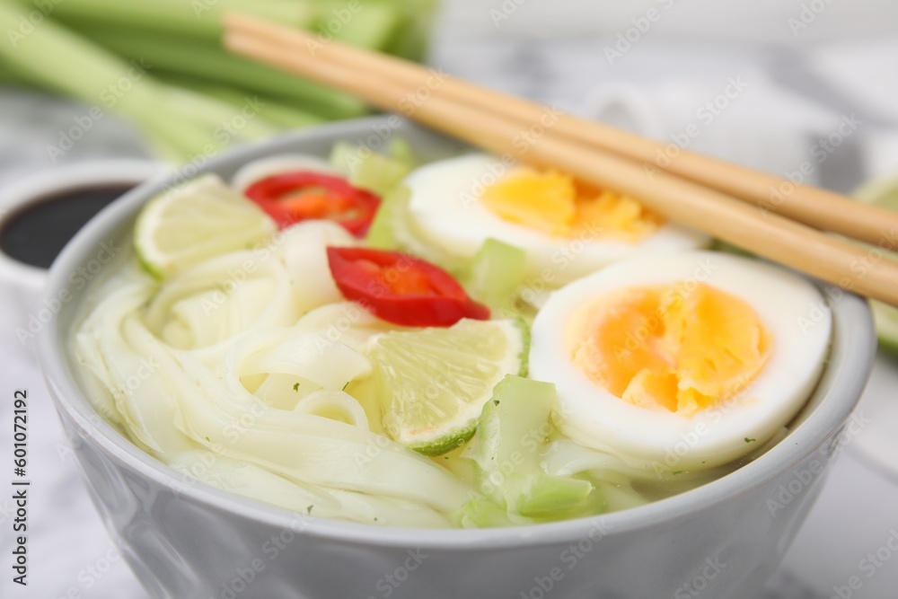Bowl of delicious rice noodle soup with celery and egg on white table, closeup Bowl of delicious rice noodle soup with celery and egg on white table, closeup