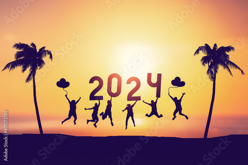 Silhouette friends jumping and holding number 2024 on sunset sky background at tropical beach. Happy new year and holiday celebration concept. Vintage tone color style.