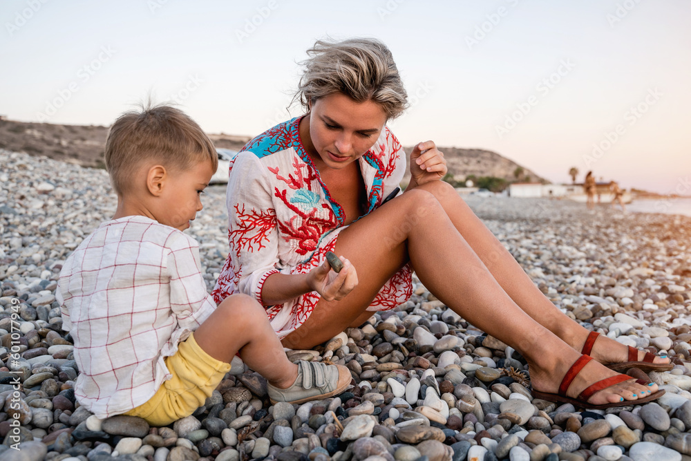 Mother and her cute little son collecting pebbles on shingle beach Mother and her cute little son collecting pebbles on shingle beach