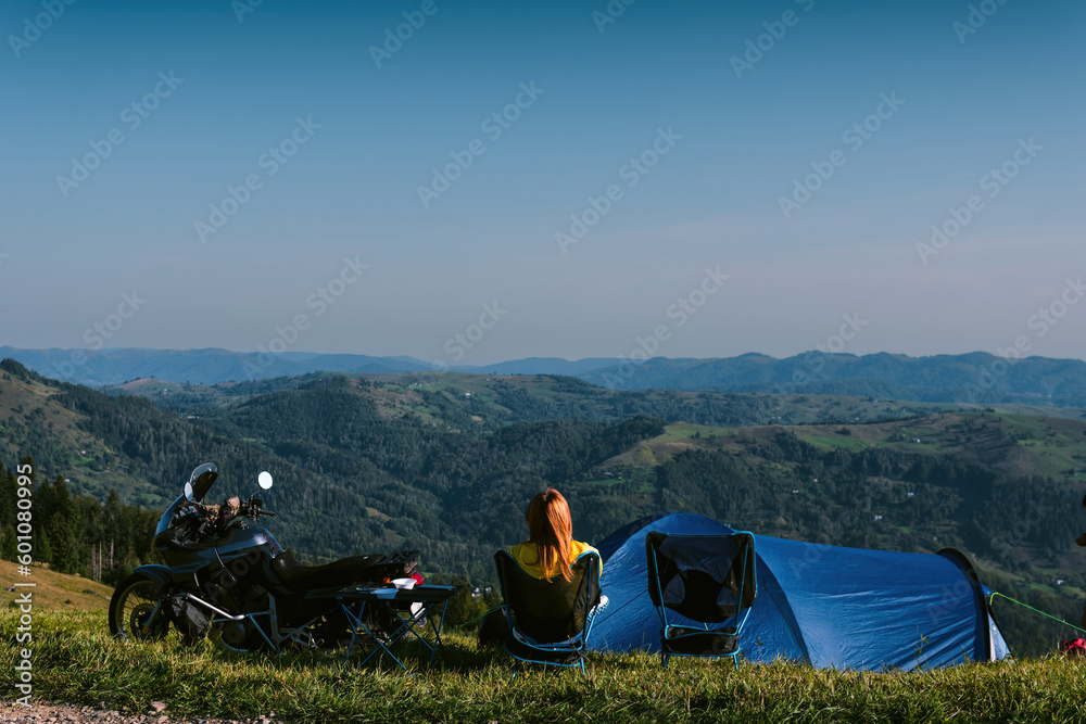 The woman is sitting alone on the folding chair. Enjoy the view. top of the mountain. adventure touring motorcycle camping equipment, off road travel vacation, tents camp. Back view