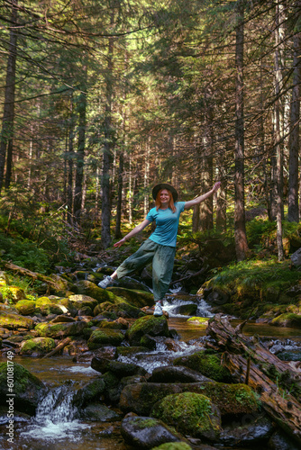 A happy woman yoga, magical, and fantastic places around the world, surrounded by nature. Female hiker crossing the river. Coniferous forest, tall Carpathian spruces. Vertical photo