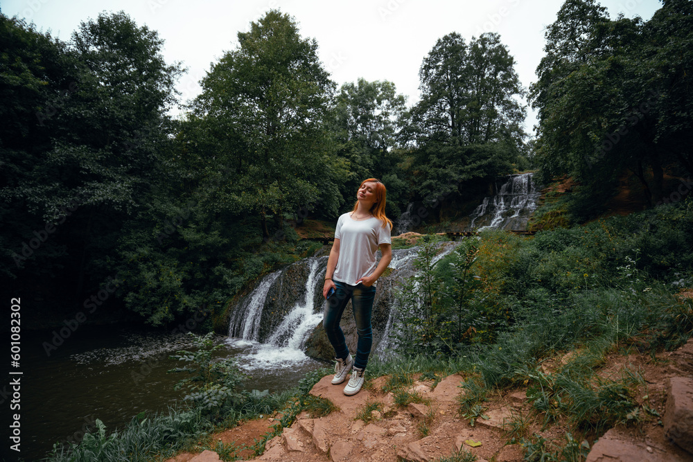 Obraz premium View of young woman standing in front of Dzhurynskyy waterfall. Female tourist, tourism and vacation, active lifestyle. Chervonogorodsky. Nyrkiv Ternopil Oblast Ukraine