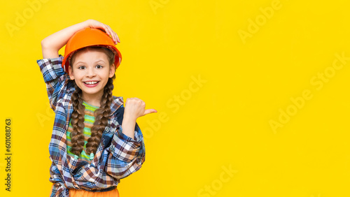 Photo A little girl in a hard hat points to your advertisement on a yellow isolated background