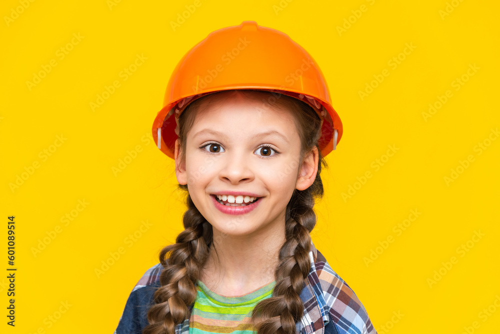 A happy little girl in a construction helmet and shirt on a yellow isolated background. The child is preparing for repairs in the nursery. The profession of an engineer. Yellow isolated background. A happy little girl in a construction helmet and shirt on a yellow isolated background. The child is preparing for repairs in the nursery. The profession of an engineer. Yellow isolated background.