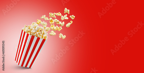Popcorn flying out of red white striped paper box isolated on red background with copy space. Splash, levitation of popcorn grains.