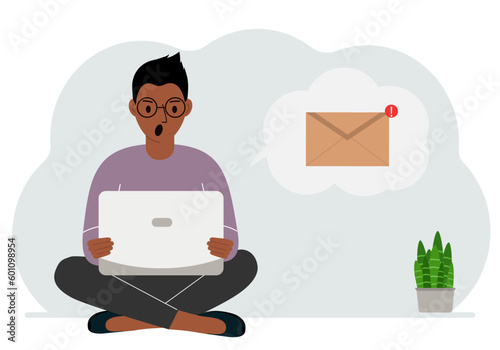 A man sits cross-legged working with a laptop and opens an email. The concept of education, work, correspondence.