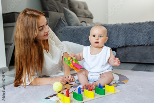 Mother and little daughter play educational games on rug in room.