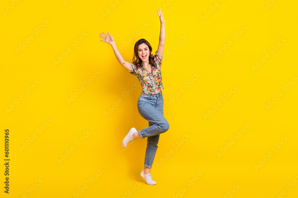 Full length photo of cheerful pretty woman dressed vintage flower print blouse dancing rising arms isolated yellow color background Full length photo of cheerful pretty woman dressed vintage flower print blouse dancing rising arms isolated yellow color background