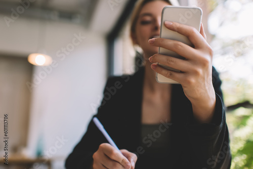 Blurred female employee using modern cellphone technology for making online booking and banking via payment application, millennial businesswoman with smartphone gadget messaging in web chat