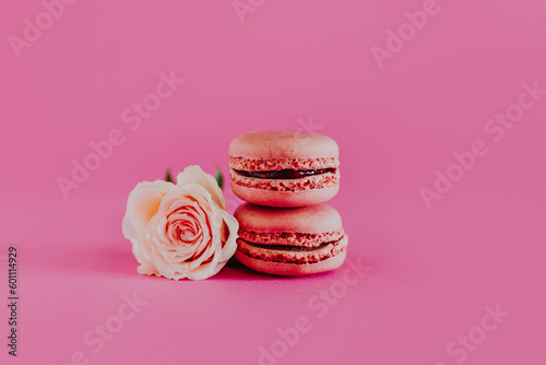 Tasty french macarons with tender rose flowers on a bright pink background.
