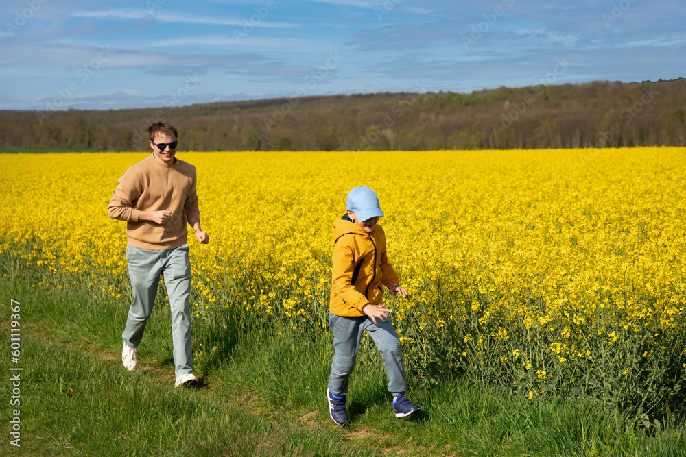 Father and son are running merrily playing in a rapeseed field, on a warm spring day. The boy and the father run and smile. front view