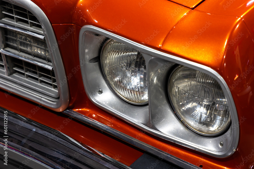 Close-up of the round headlamps of a orange american classic car. Natural patine on the chrome details of a historic vehicle.