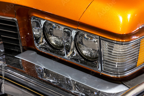 Close-up of the round headlamps of a orange american classic car. Natural patine on the chrome details of a historic vehicle.