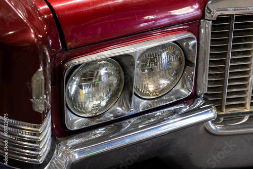 Close-up of the round headlamps of a red american classic car. Natural patine on the chrome details of a historic vehicle.