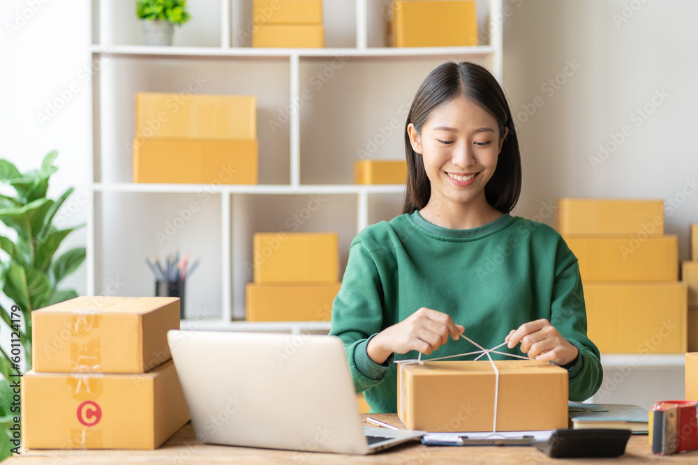An excited Asian female small business owner works in her room while using her laptop computer to take orders and deliver packages. SME business idea An excited Asian female small business owner works in her room while using her laptop computer to take orders and deliver packages. SME business idea