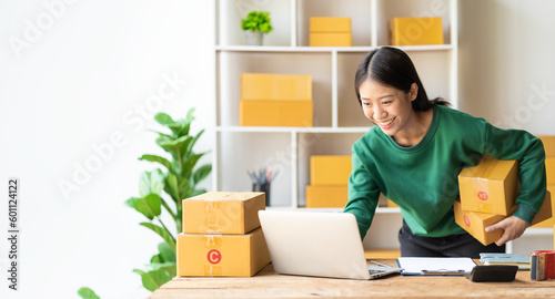 An excited Asian female small business owner works in her room while using her laptop computer to take orders and deliver packages. SME business idea