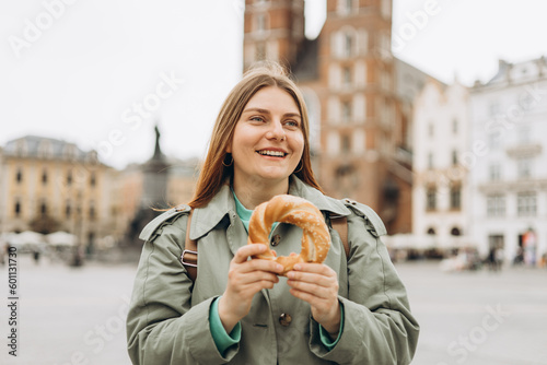 Attractive young female tourist is holding prezel  traditional polish snack on the Market square in Krakow. Traveling Europe in spring. High quality photo