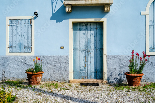 Old wall of a sunlit blue painted house with wooden door and balcony. Textures