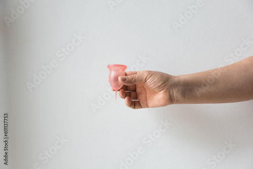 female hand holds pink reusable silicone menstrual cup, on white background, alternative feminine hygiene for period or menstrual cycle 