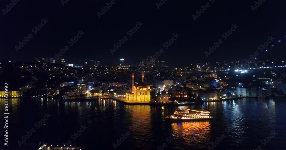 Aerial view of Ortakoy Mosque and flying over an illuminated tour boat at night. Buyuk Mecidiye Camii well known as Ortakoy Mosque and it's located in an amazing place by the waters close to Bosphorus Aerial view of Ortakoy Mosque and flying over an illuminated tour boat at night. Buyuk Mecidiye Camii well known as Ortakoy Mosque and it's located in an amazing place by the waters close to Bosphorus