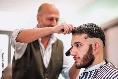 Barber trimming hair of man in barbershop