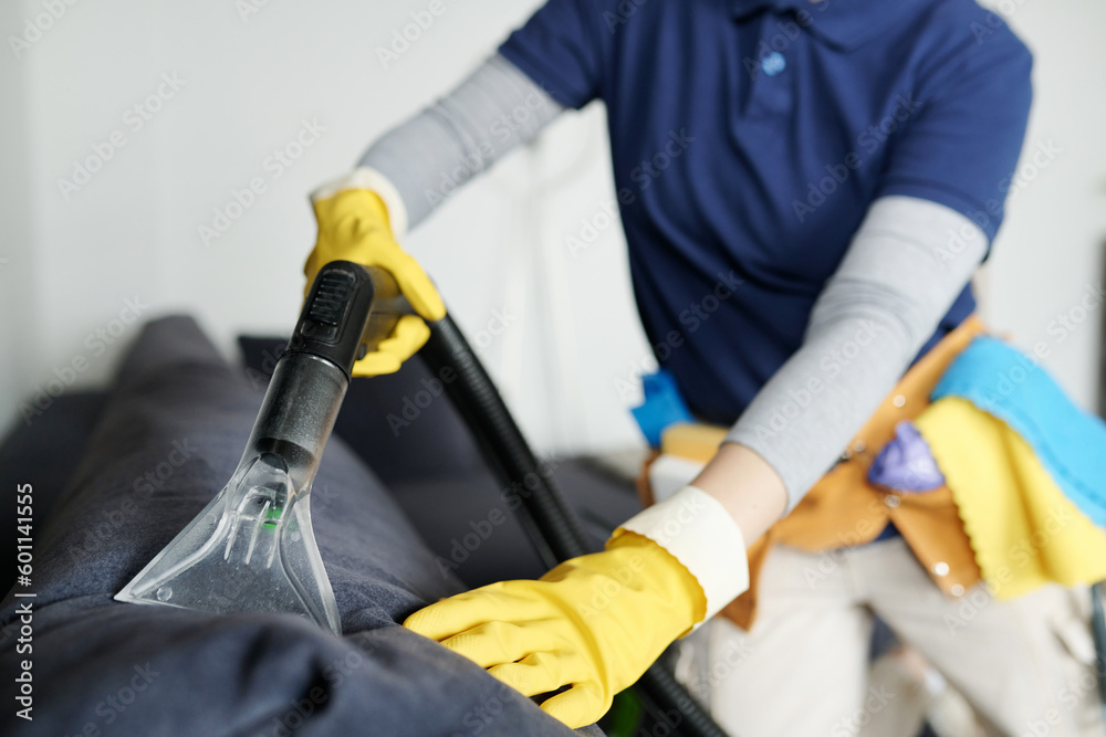 Close-up of worker in protective gloves vacuuming furniture in the room