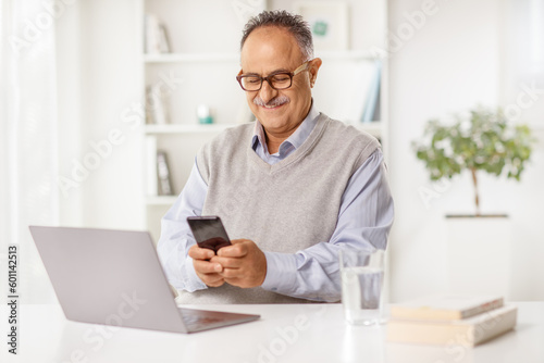 Mature man sitting at desk with a laptop computer and using a smartphone