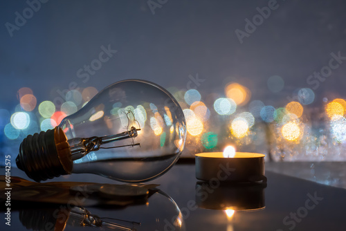 Tablou canvas Incandescent lamp and candle on the background of city lights