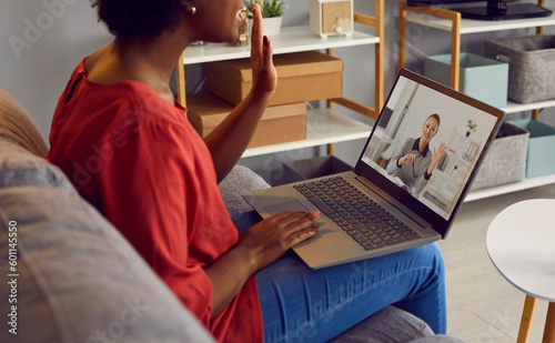 African American woman sitting on sofa at home, looking at laptop computer screen, and greeting her psychotherapist at video conference meeting session. Remote psychotherapy, online therapy concept photo