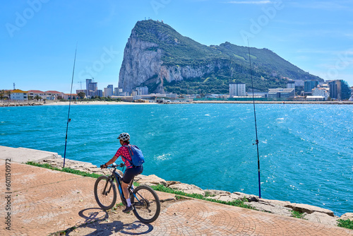 happy senior woman cycling with her electric mountain bike below the Rock of Gibraltar, Andalusia, Spain