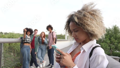 concept of bullying students, group of young people laugh at a girl who is using her smart phone