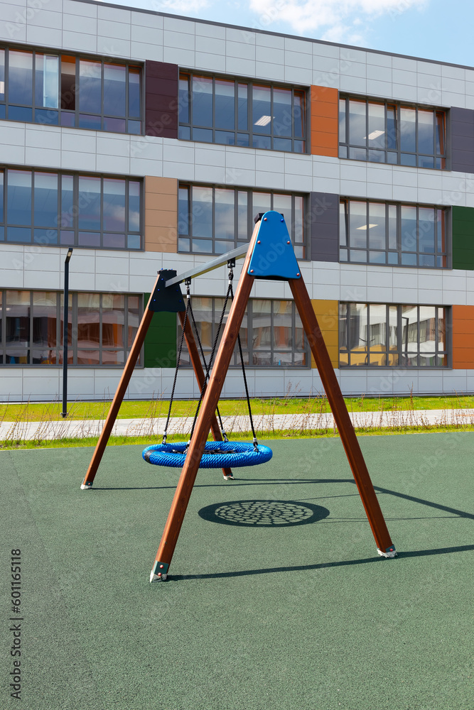 Fototapeta premium Outdoor swing with wicker round seat on green artificial ground. School playground