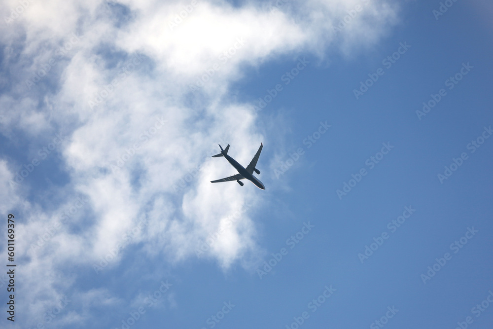 Silhouette of airplane flying in sky with white clouds. Passenger plane at flight, travel concept