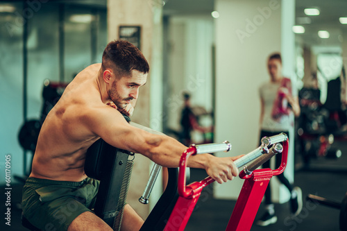 A shirtless sportsman in shape is reaching for a handle on an exercise machine in a gym.