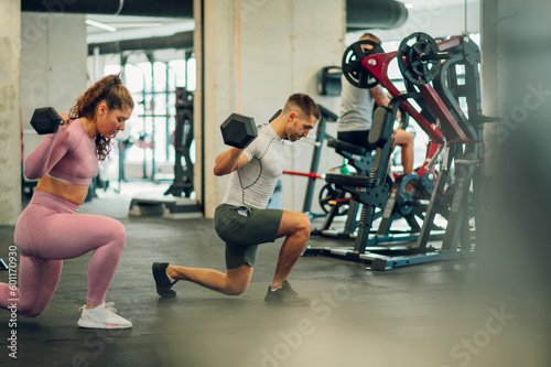 Full length of a strong couple doing lunges while lifting dumbbells in a gym.