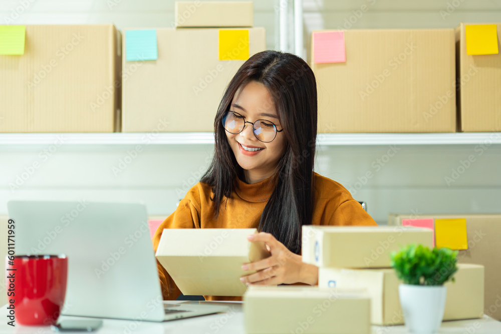 Young Asian woman prepare parcel box and check online orders of product for deliver to customer on laptop computer. Shopping Online concept. Young Asian woman prepare parcel box and check online orders of product for deliver to customer on laptop computer. Shopping Online concept.