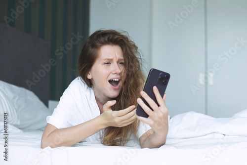 young happy woman use phone and lying in bed in bedroom in the morning, concept morning, phone addiction, social, habits