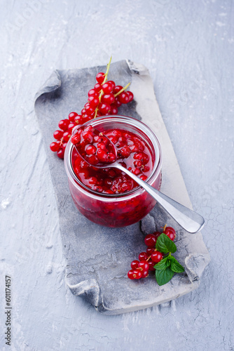 Ripe red currant from organic cultivation and marmalade offered as a close-up on a gray design ceramic tray with copy space