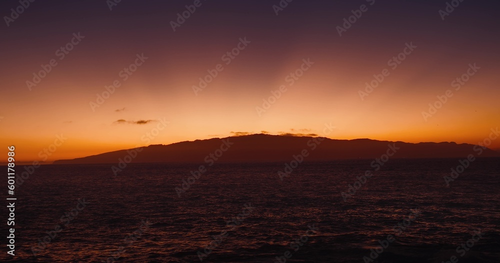 Island silhouette in ocean in magical sunset lilac light. Sky glows like in a fairy tale. La Gomera, Canary, Spain. Dark sea water at dusk. Island silhouette in ocean in magical sunset lilac light. Sky glows like in a fairy tale. La Gomera, Canary, Spain. Dark sea water at dusk.